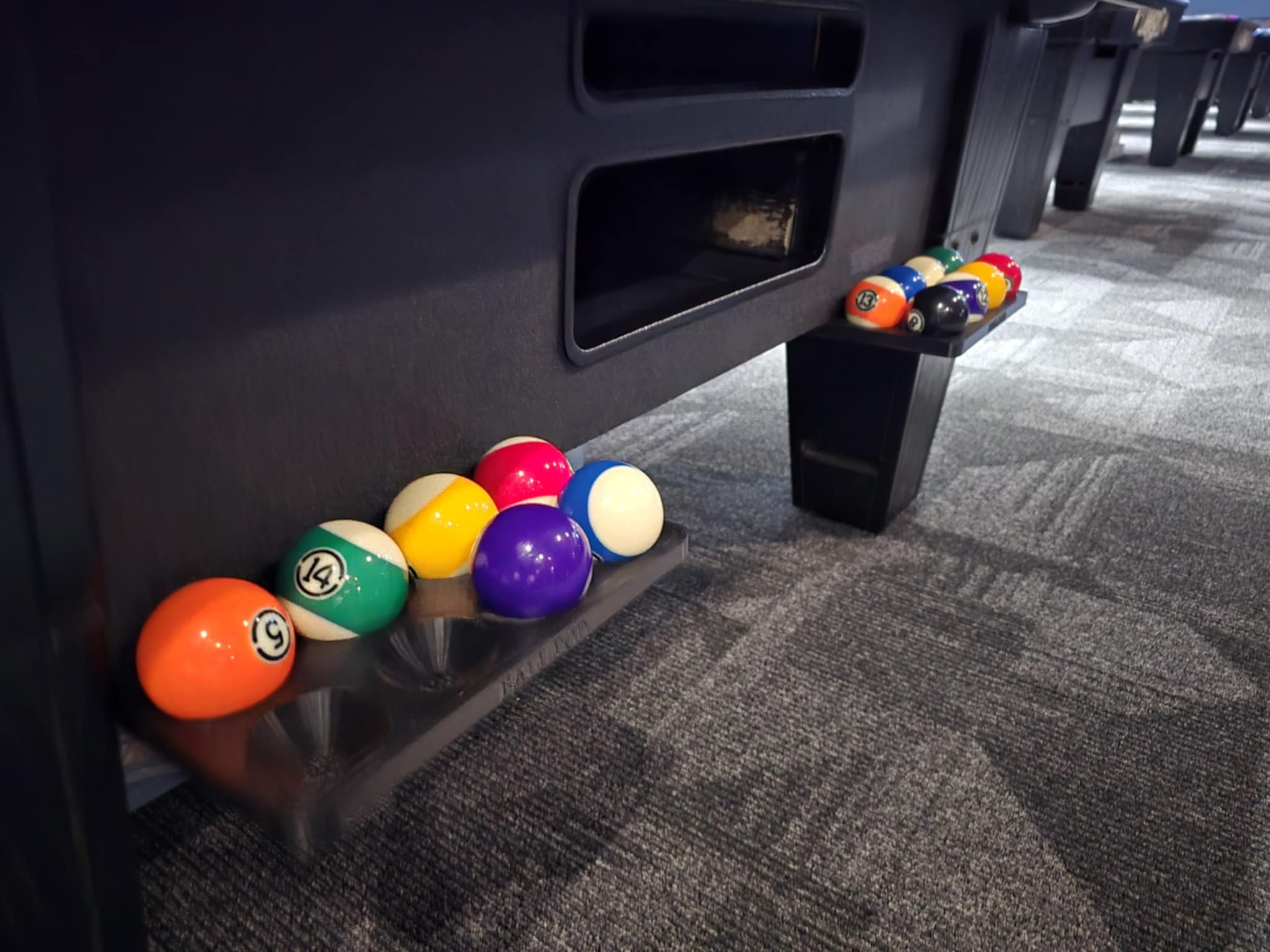 The Original Ball Pod with eight spare billiard balls neatly stored beside a pool table.